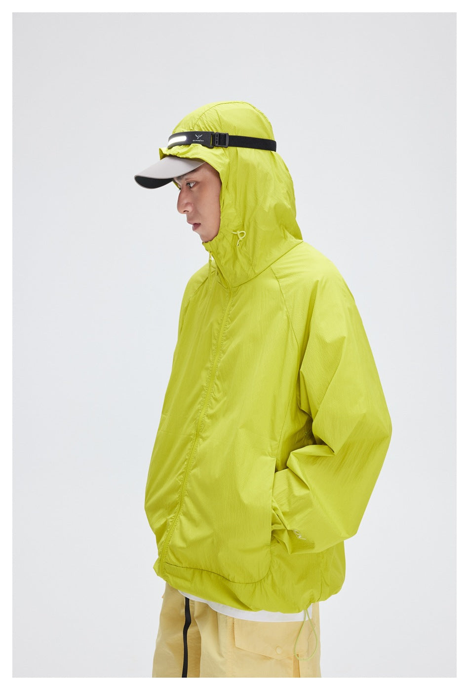 Side view of a person wearing a bright lime-yellow hooded jacket and beige cap with a black strap.