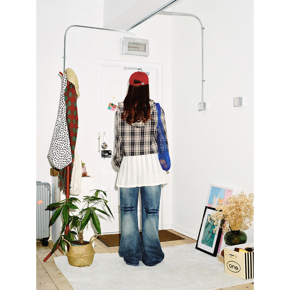 Rear view of a model wearing a gray plaid hooded top, white pleated layer, and wide-leg jeans.