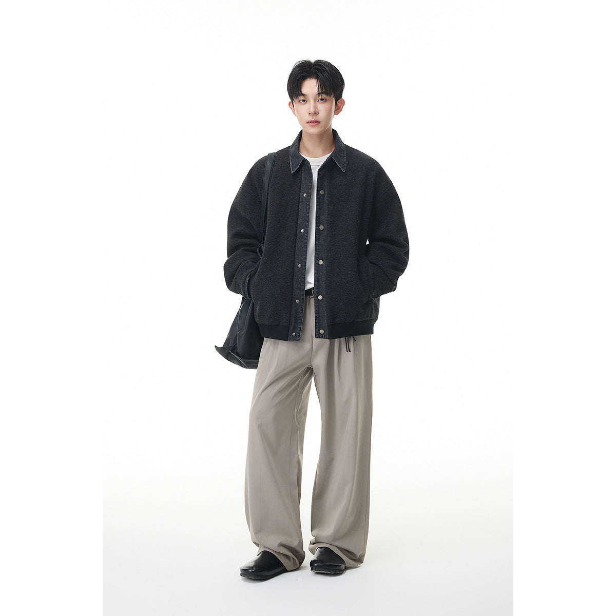 Full-length front view of a model wearing a charcoal button-front jacket with denim trim and loose light trousers.