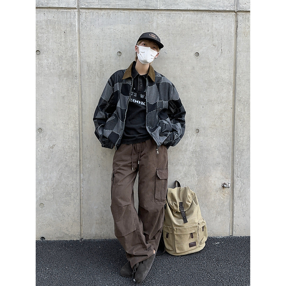 Model wearing a charcoal patchwork zip jacket, black graphic shirt, loose brown cargo pants and a black cap.