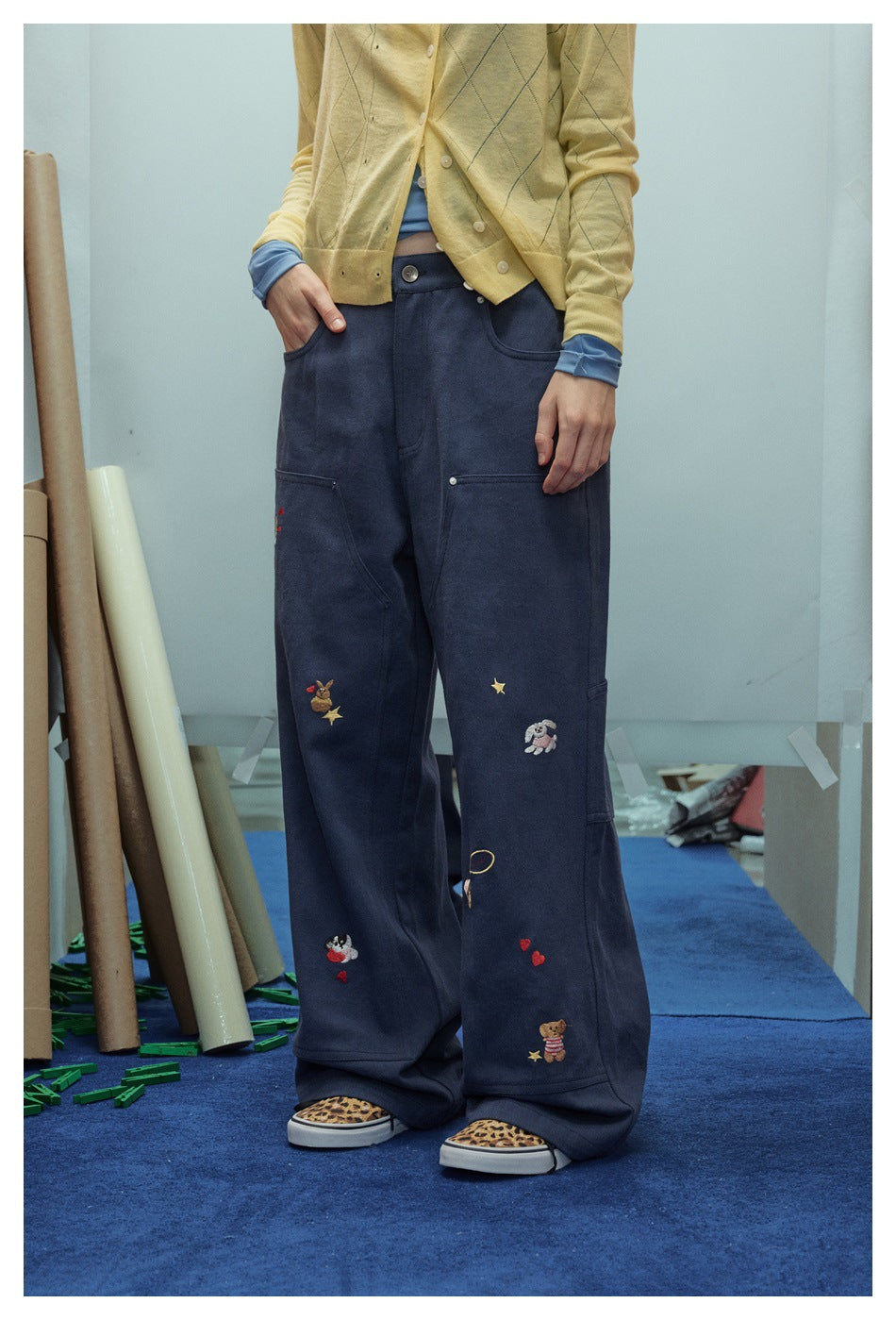 Front view of a model wearing navy wide-leg utility pants decorated with colorful embroidered characters and stars.