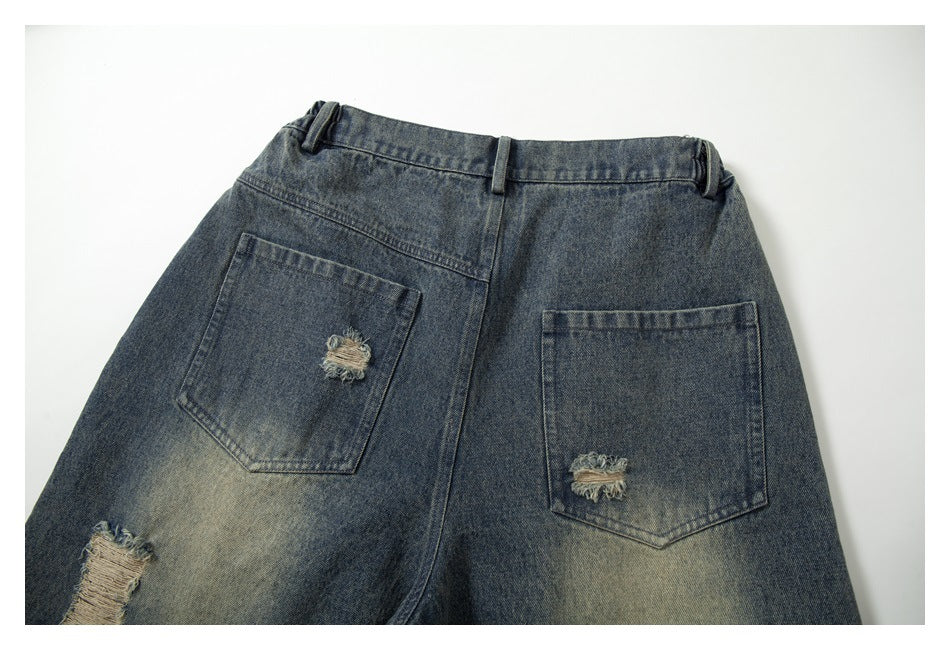 Close view of the back of faded dark blue jeans with belt loops, two distressed pockets, and a frayed tear.