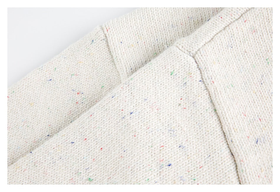 Close-up of an off-white knit garment with small multicolored flecks and overlapping seam edges.