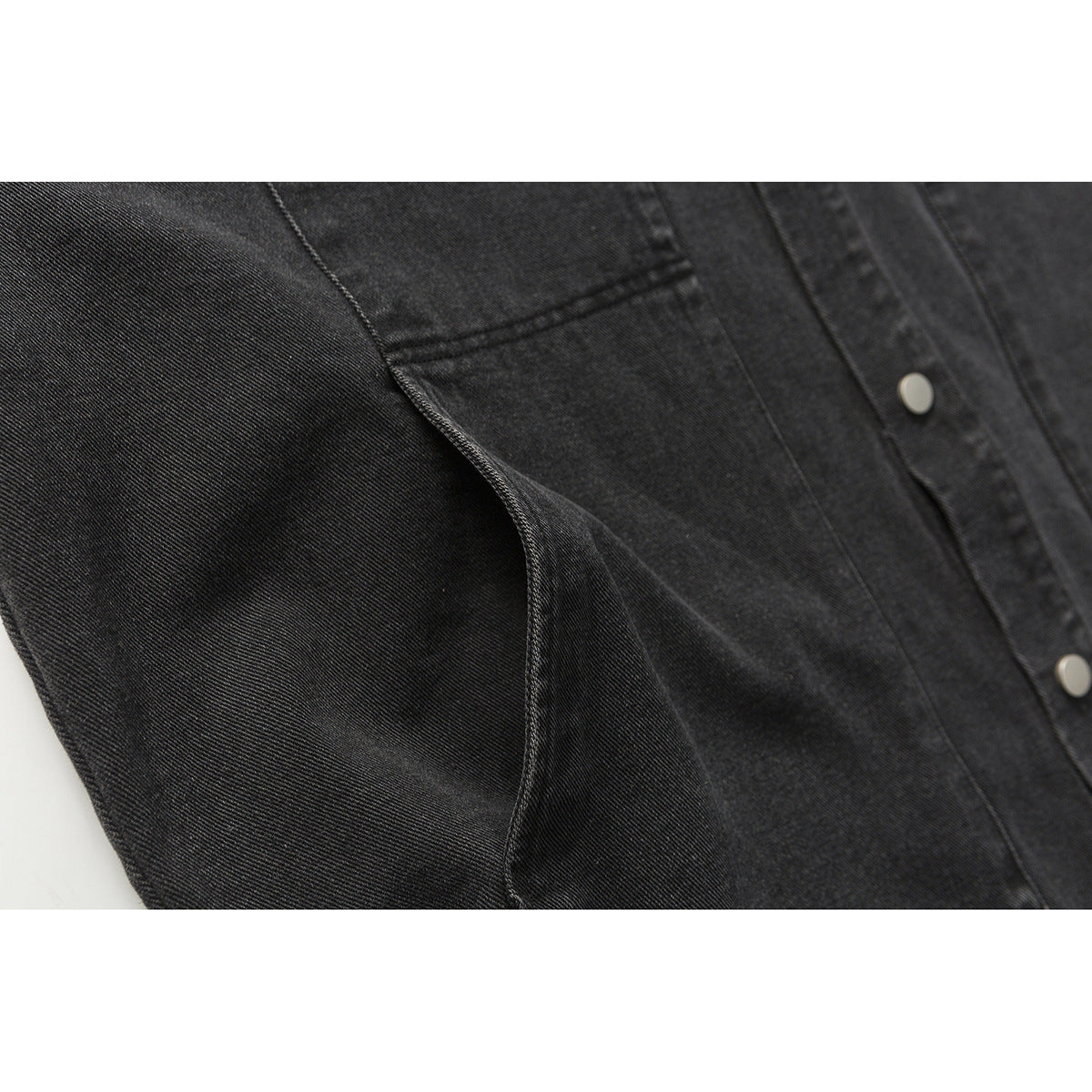 Close-up of a black denim jacket sleeve seam and front snap-button placket.