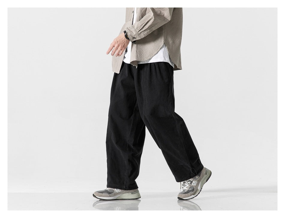 Model walking in black wide-leg pants with a beige ribbed shirt and gray sneakers, side view