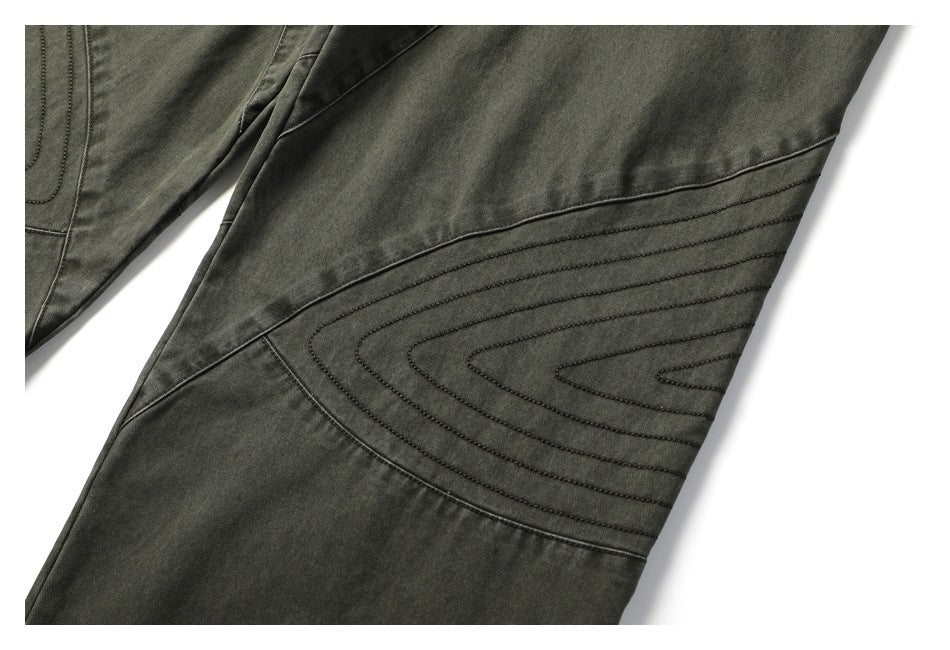 Close-up of a pants leg showing curved, parallel stitched panels on dark olive-gray fabric.