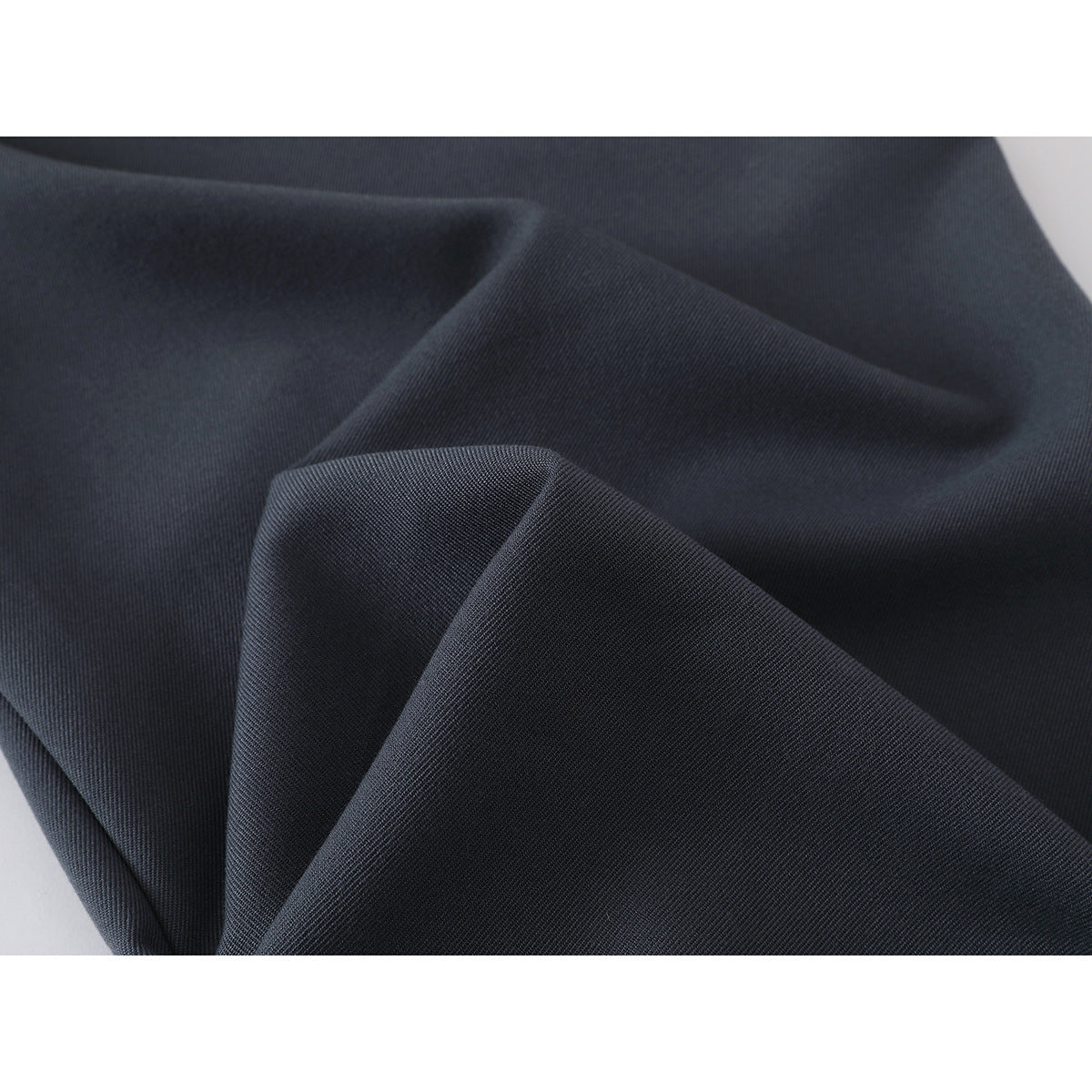 Close-up of dark charcoal trouser fabric folded to show its fine diagonal texture.