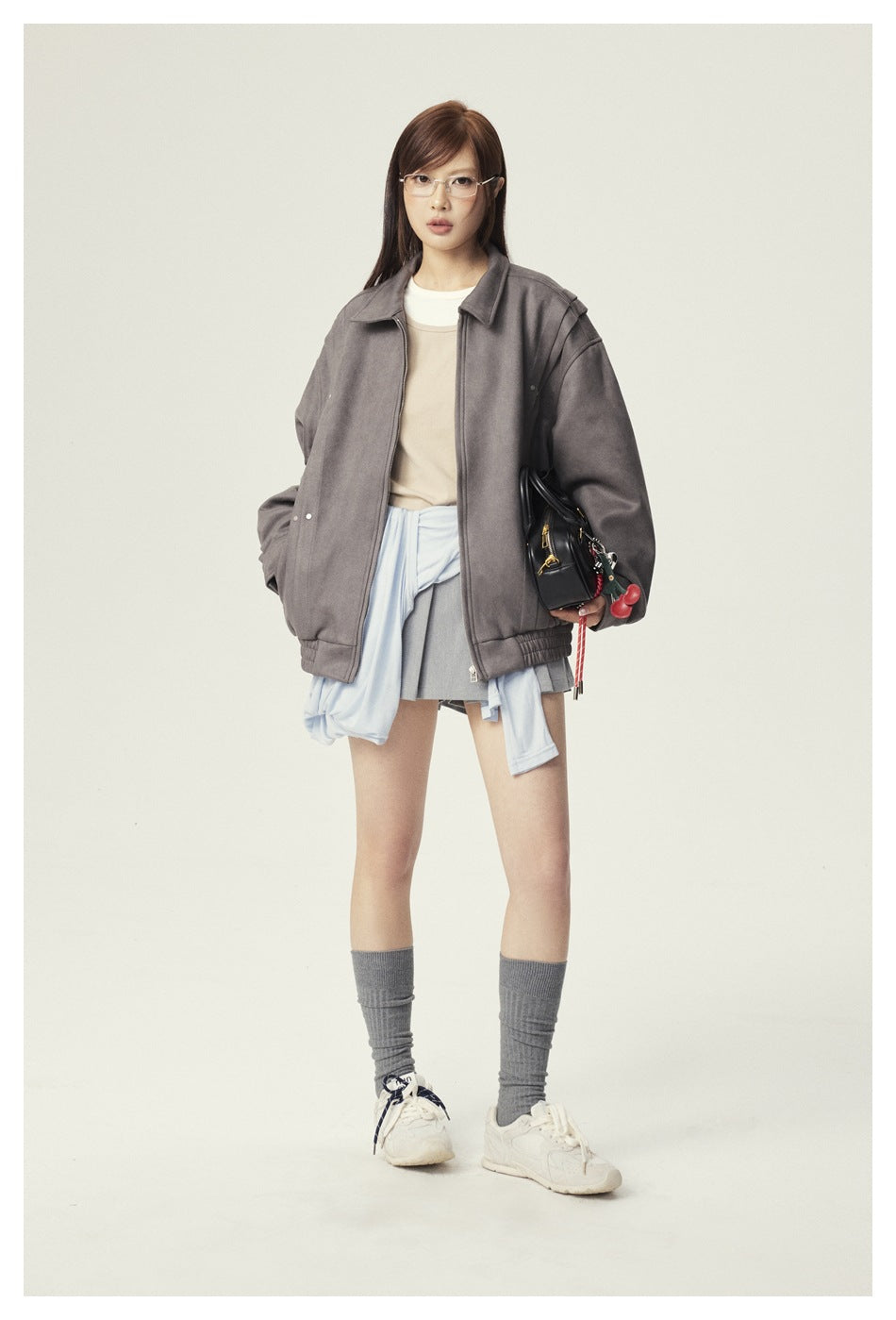 Full-length model wearing an oversized gray zip jacket, beige top, gray skirt, and sneakers.