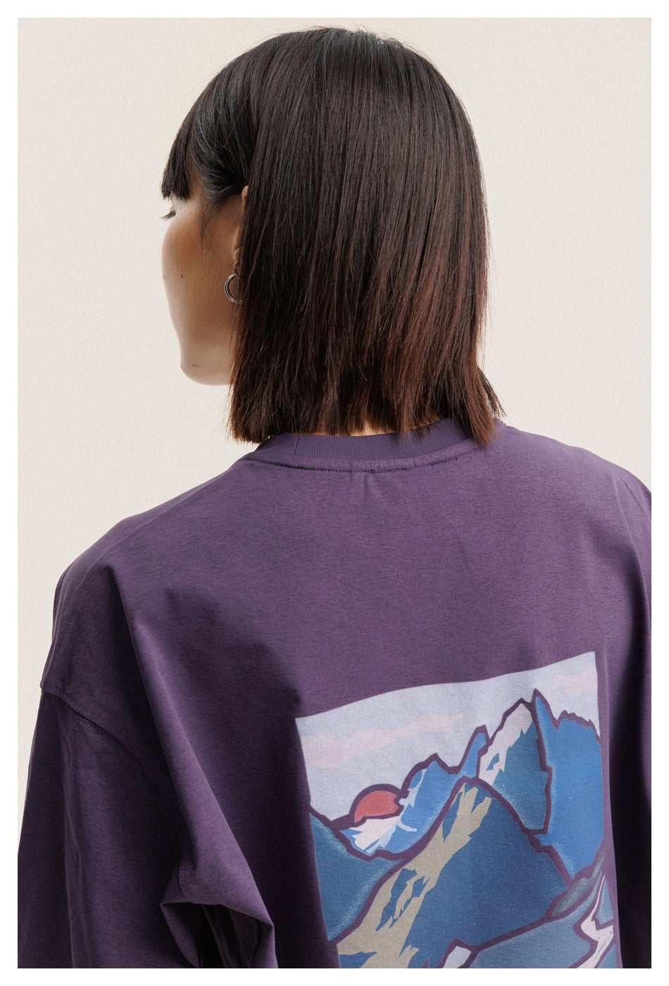 Rear view of a model wearing a purple long-sleeve shirt with a large colorful mountain graphic.