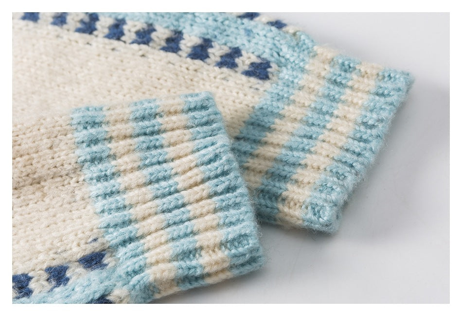Close-up of cream knit sweater cuffs with pale blue and navy geometric patterned bands.