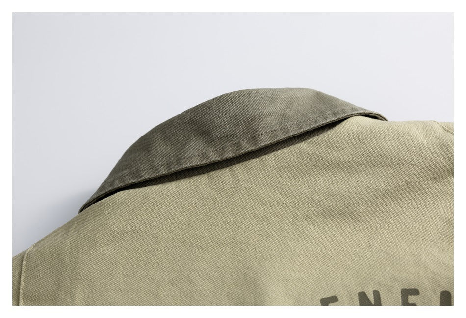 Close-up of a khaki garment collar and shoulder, with part of a dark printed design visible at the lower edge.