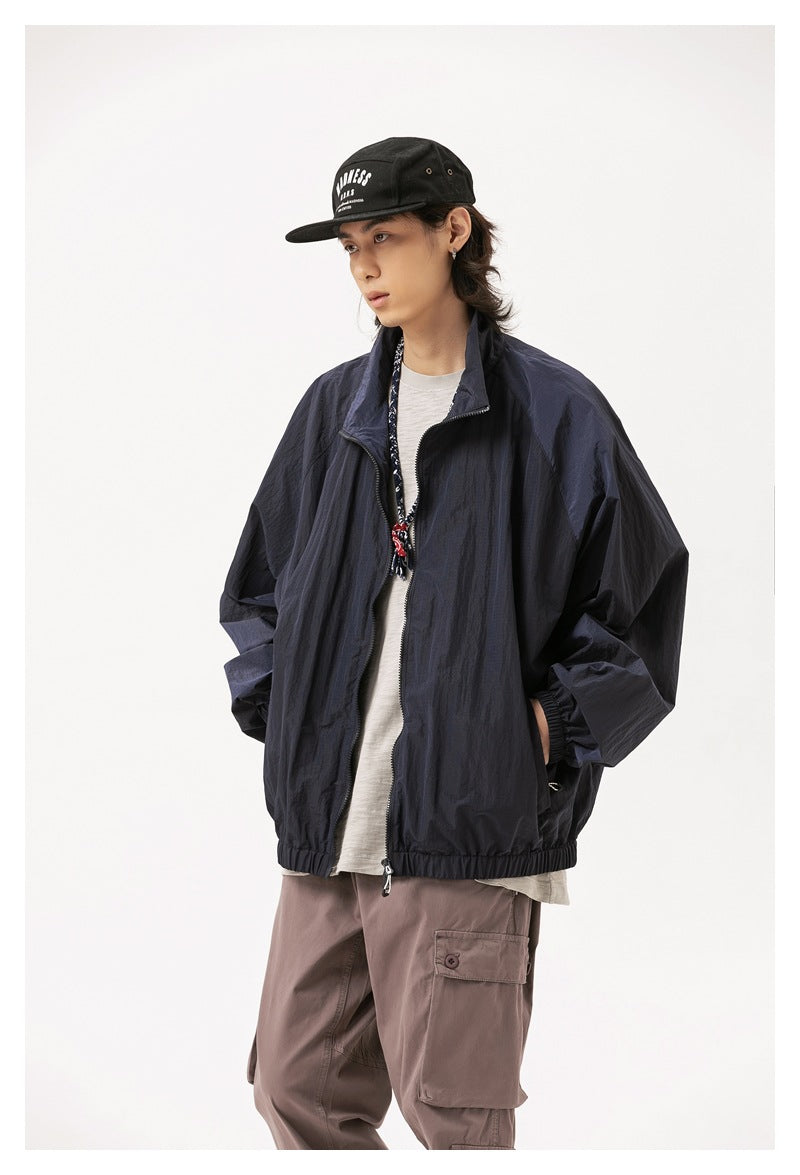Model wearing a dark navy zip-front jacket with a high collar and elastic hem, styled with a black cap and mauve cargo pants.