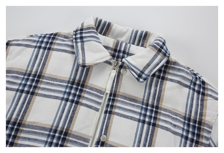 Close-up of a cream plaid jacket's pointed collar, front zipper, and silver snap buttons.