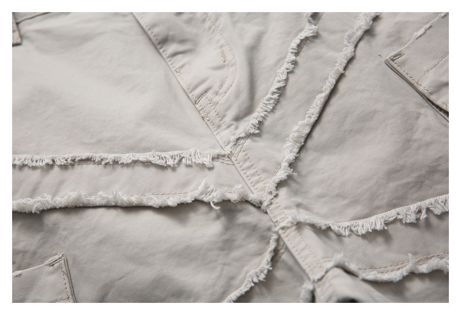 Close-up of overlapping frayed fabric panels and stitching on light taupe trousers.