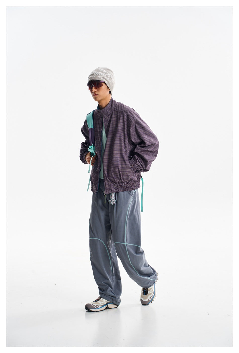 Model wearing a purple checked jacket, teal shirt and loose slate trousers with turquoise piping.