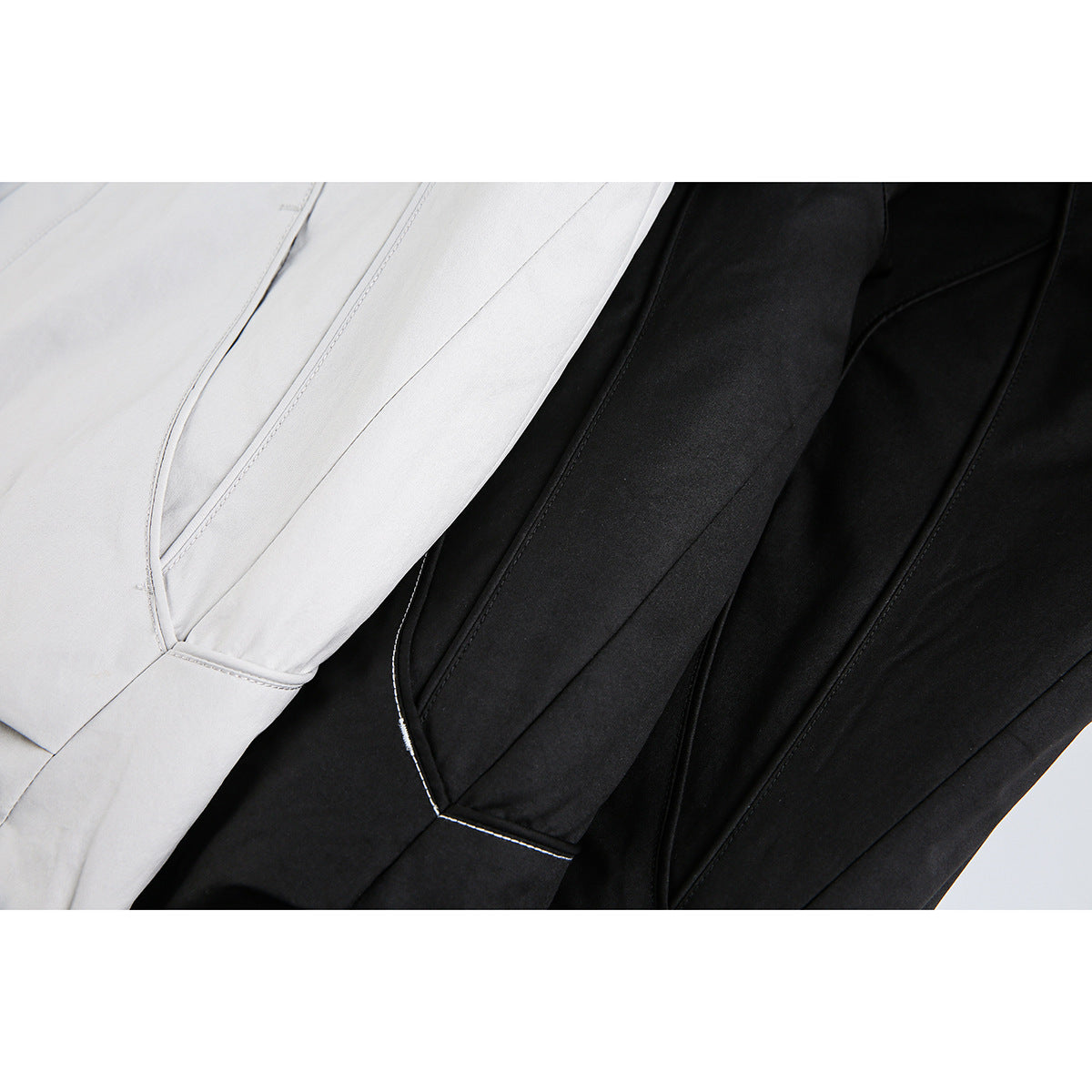 Close-up of light gray and black jacket panels with curved seams and contrast topstitching.