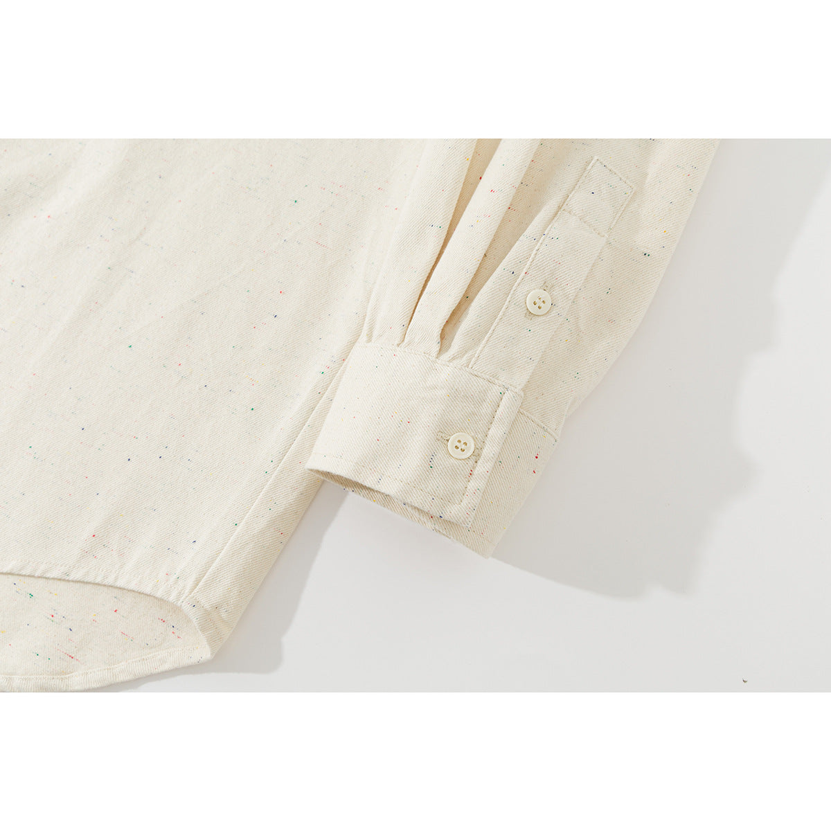 Close-up of an ivory speckled shirt sleeve and buttoned cuff laid against a light background.