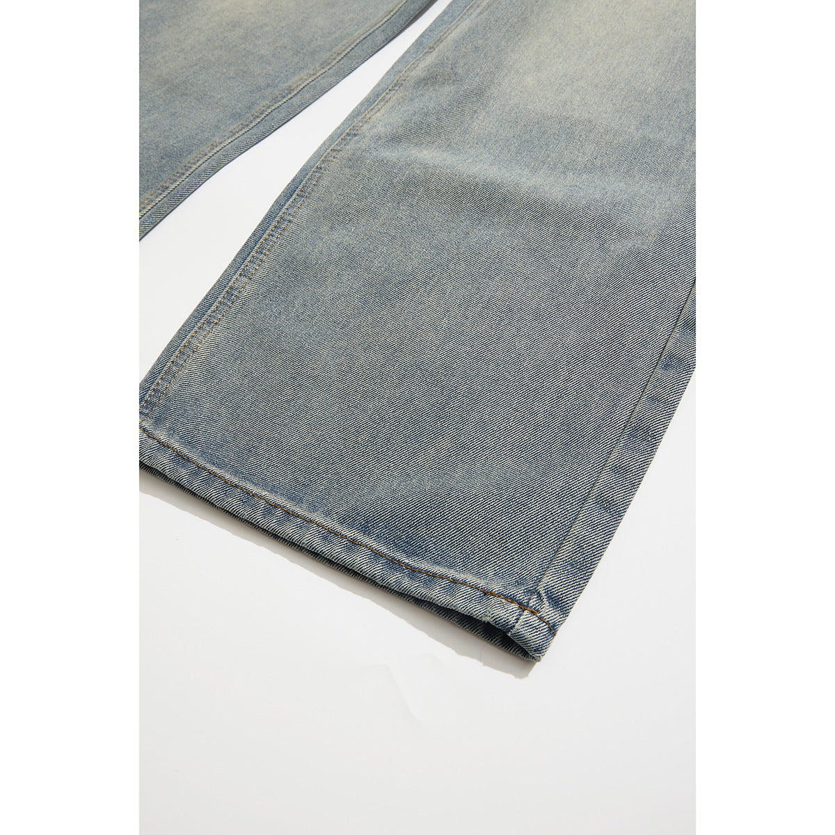 Close-up of the light blue jeans leg and stitched hem laid flat against a white background.