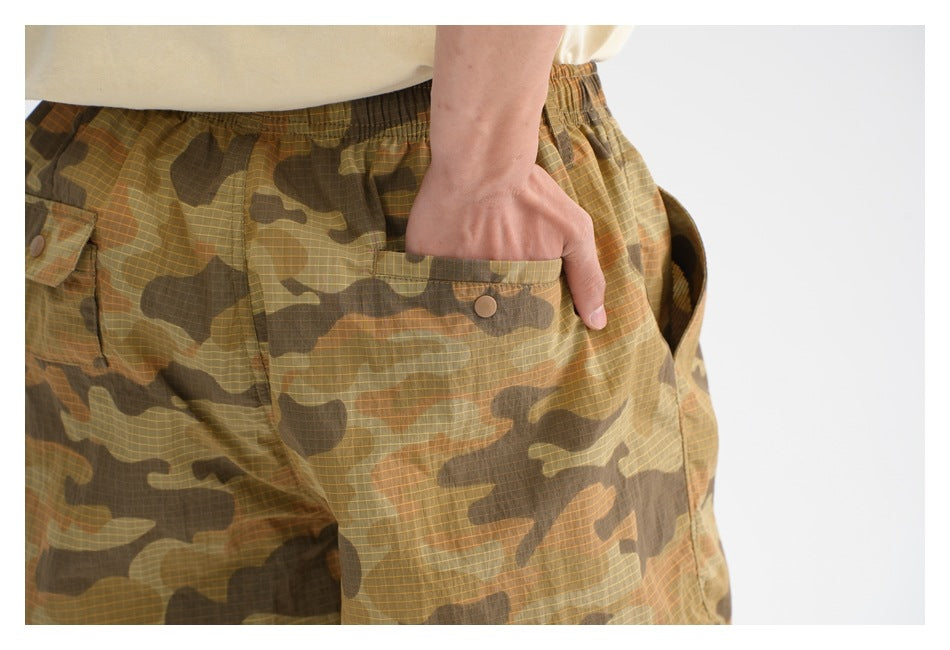 Close-up of a person wearing olive and brown camouflage shorts, showing a large button-flap side pocket.