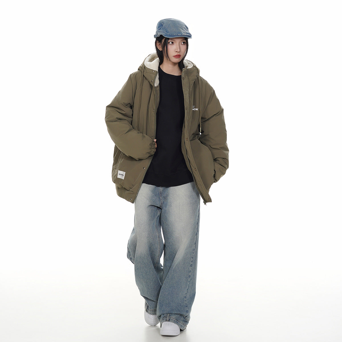 Model wearing an olive hooded jacket with cream lining, a black top, and loose light-wash jeans.