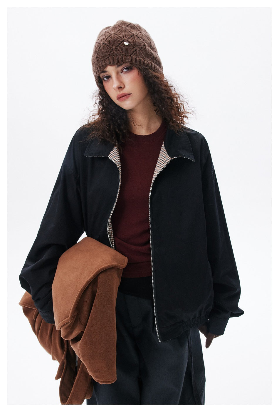 Closer view of a model in a black jacket with checked lining, burgundy top and brown knit beanie.