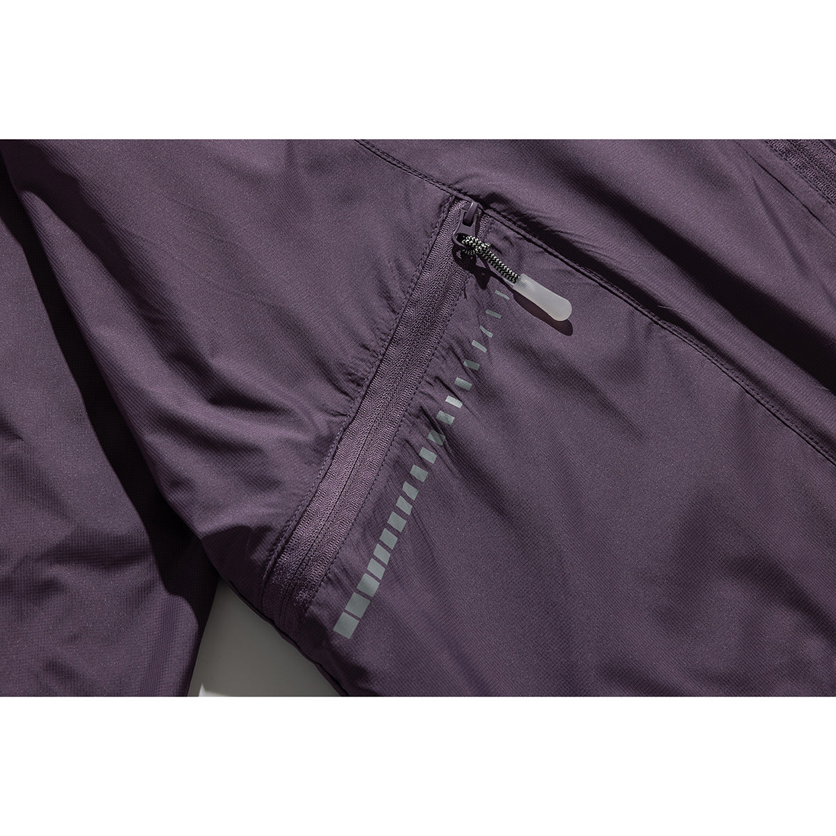 Close-up of a purple jacket pocket zipper with a pull tab and reflective segmented trim.