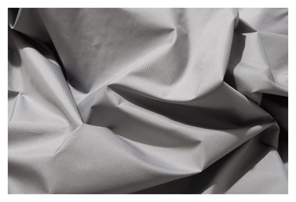 Close-up of light gray fabric with a fine grid texture arranged in soft folds.