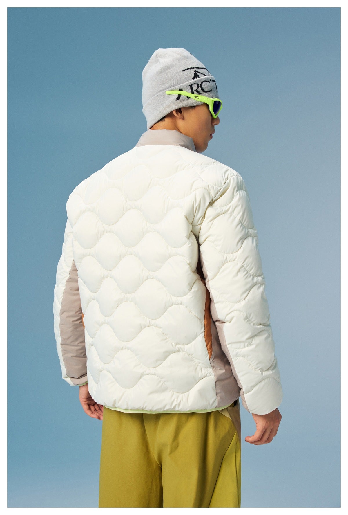 Back view of a model wearing a white wave-quilted jacket with taupe side panels and sleeves.