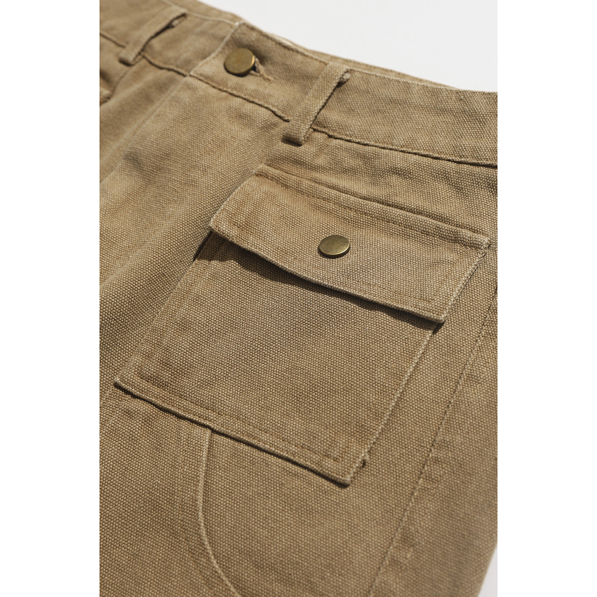 Close-up of tan shorts highlighting a large snap-button flap pocket and textured fabric.