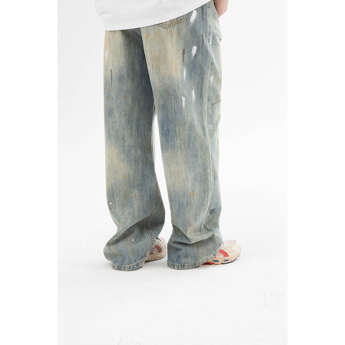 Rear view of wide, faded blue jeans with scattered distressed marks and a back pocket, worn by a model.