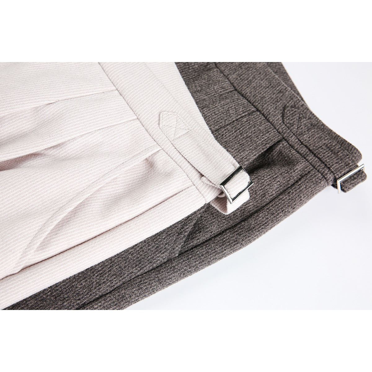 Close-up of ivory and charcoal trouser side tabs with rectangular metal buckles and textured fabric.