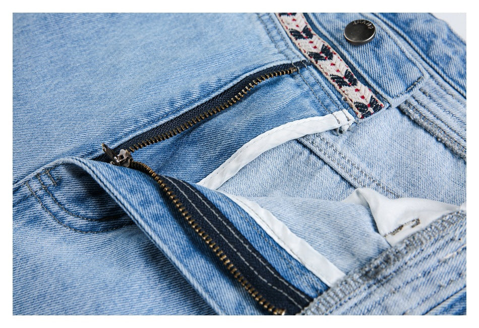Close-up of light-wash jeans with the zipper open, revealing the fly and white inner waistband lining.