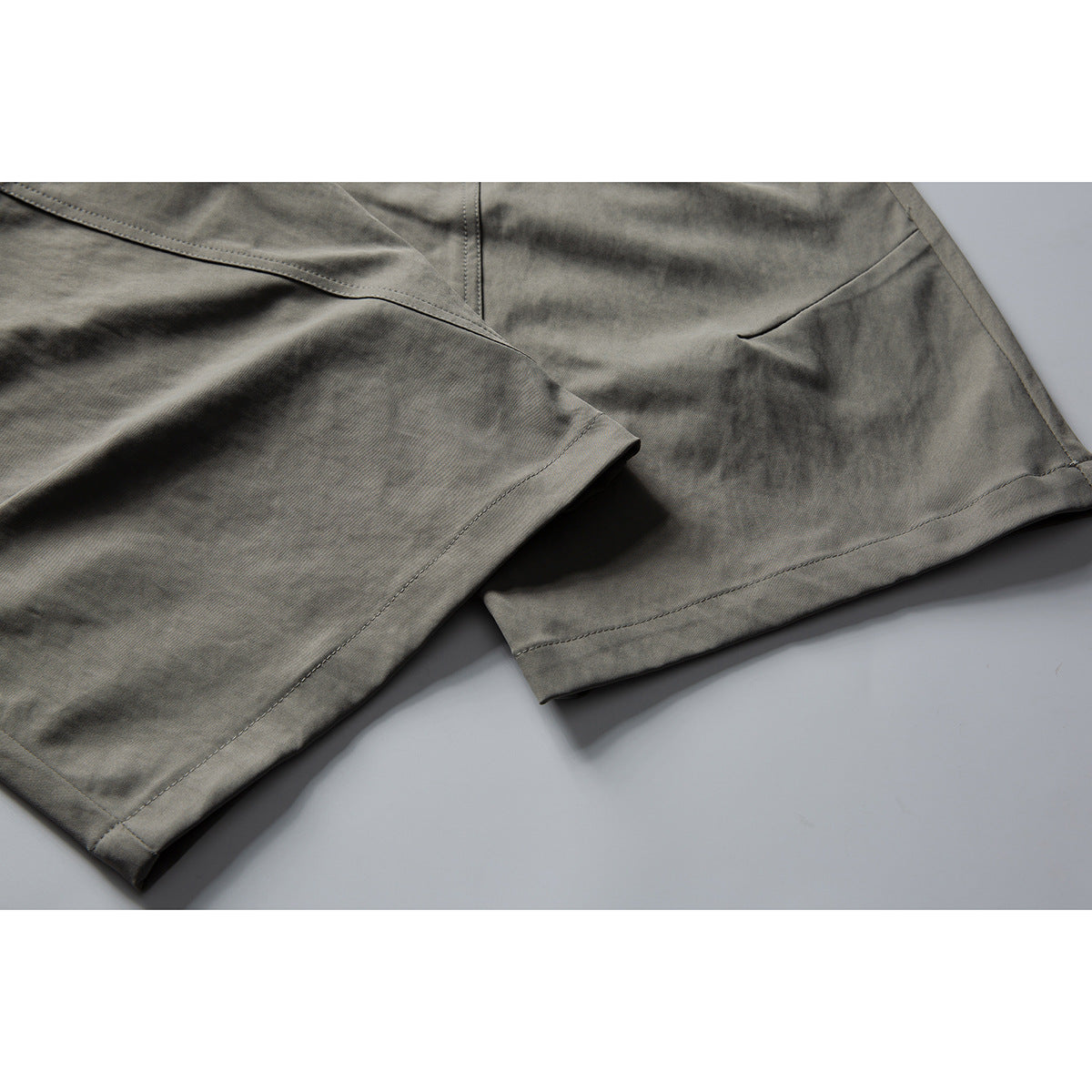 Close-up of gray trouser legs showing stitched hems, seams, and a pocket opening.