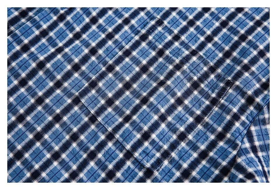 Close-up of a stitched chest pocket on blue, black, and white plaid shirt fabric.
