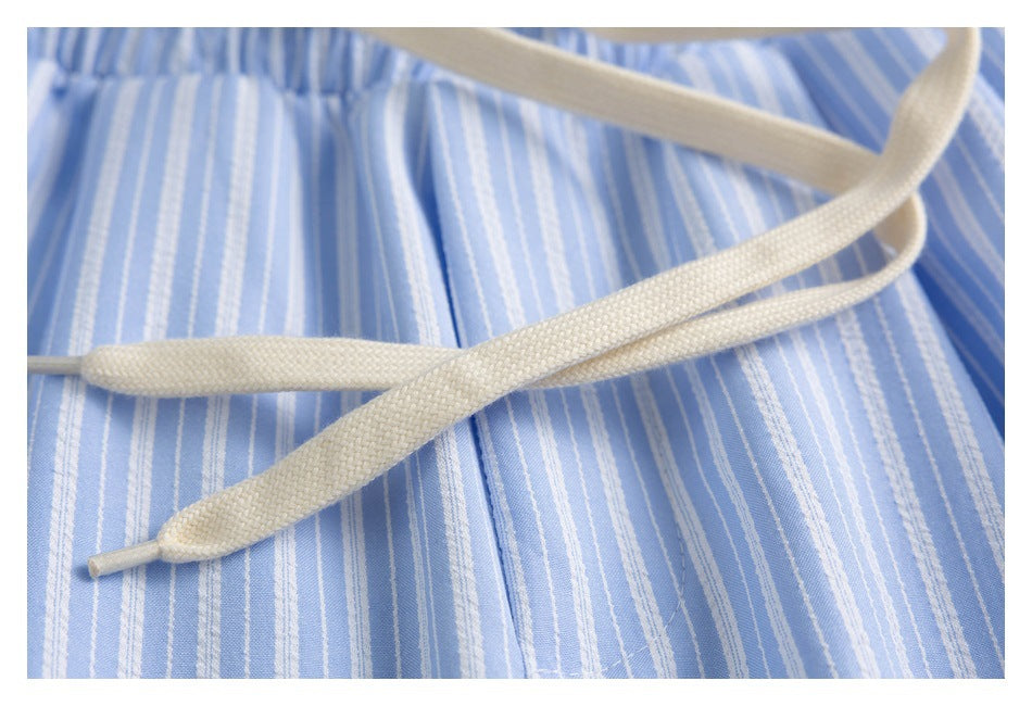 Close-up of a cream drawcord crossing light blue shorts with narrow white stripes.