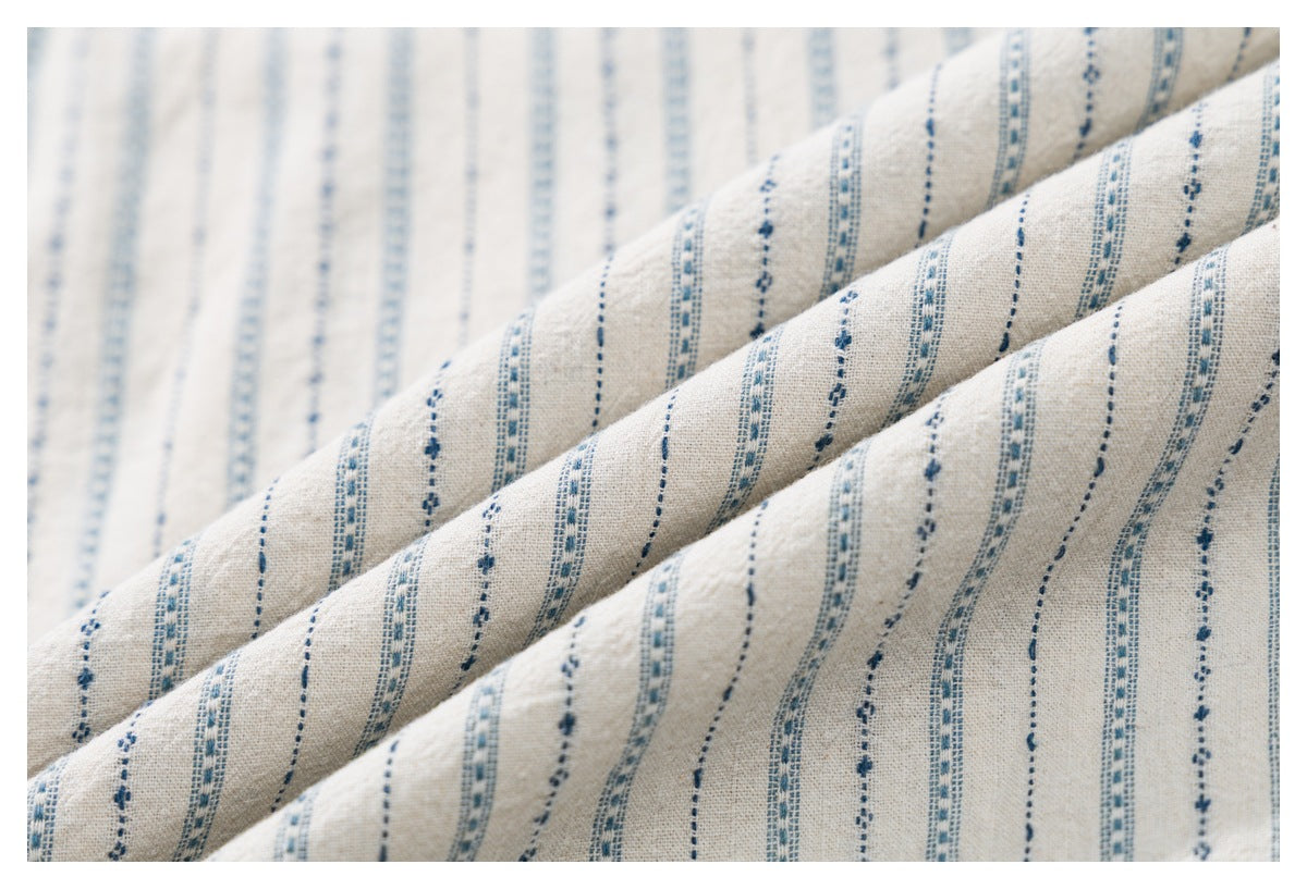 Close-up of off-white fabric draped in folds, patterned with narrow blue stripes.