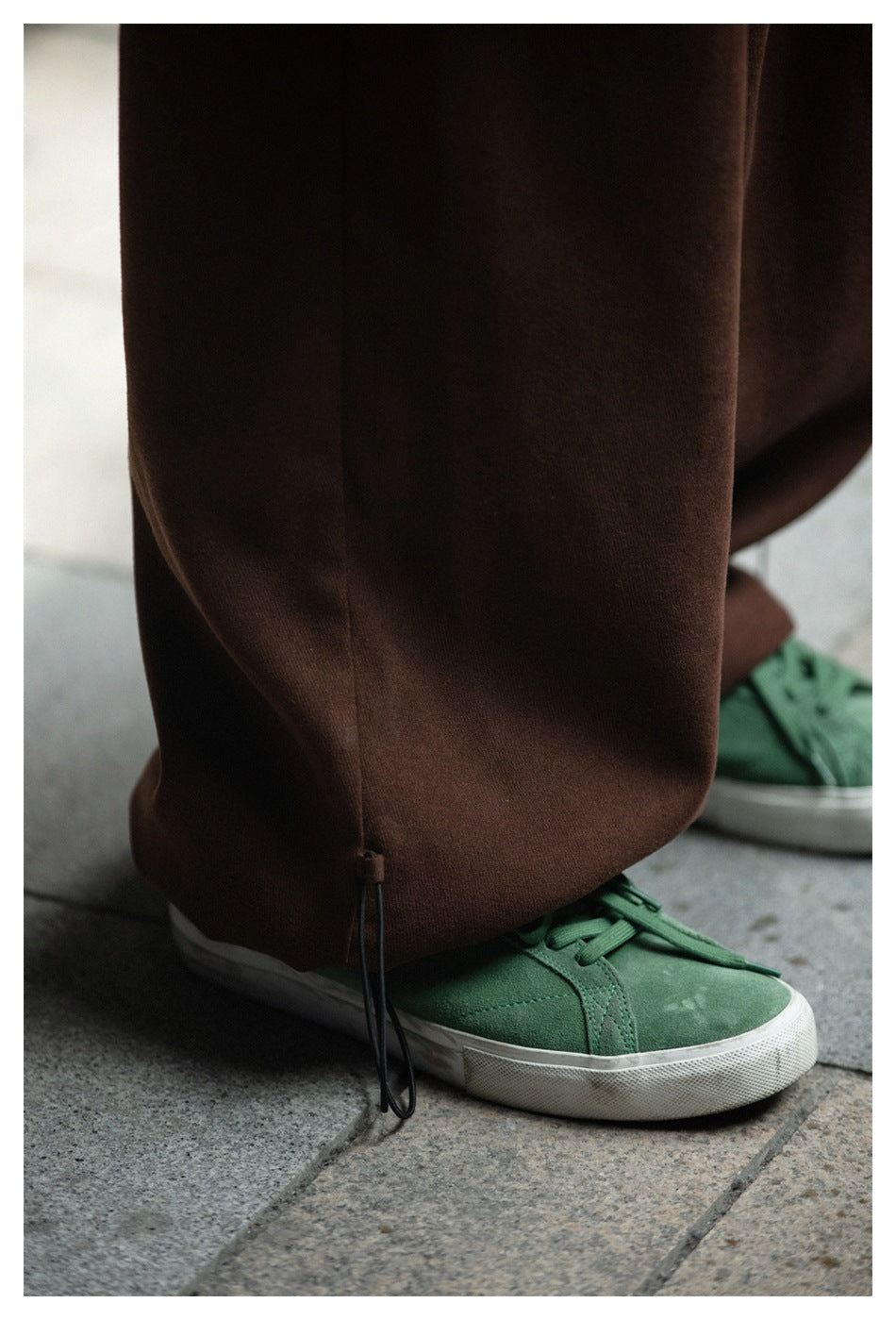 Close-up of brown wide-leg trousers with an adjustable drawcord hem, worn over green sneakers.