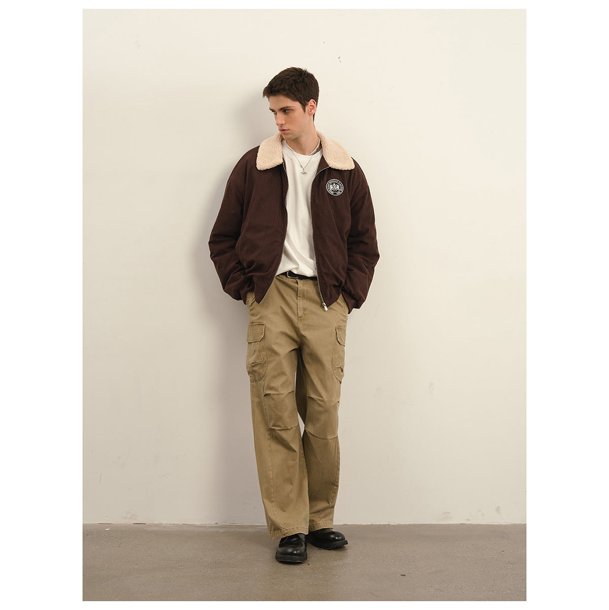 Model wearing a dark brown zip jacket with a cream sherpa collar, white shirt, and khaki cargo pants.