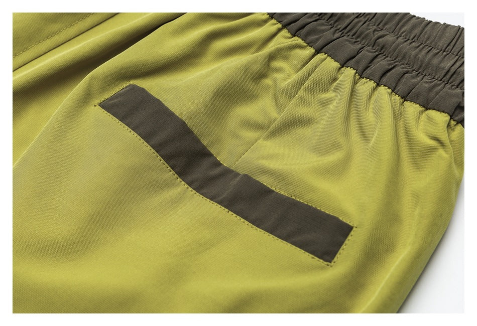 Close-up of a dark-trimmed pocket on yellow-green shorts beside the gathered dark waistband.