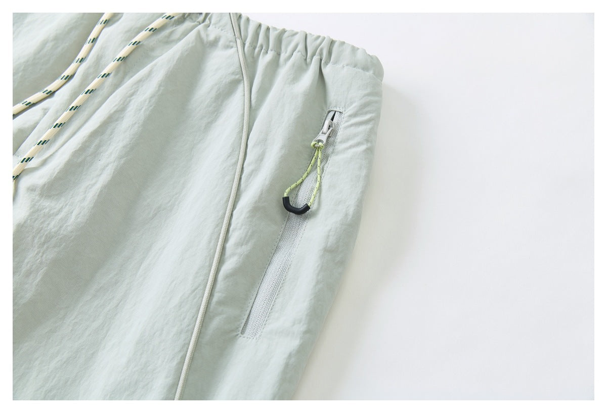 Close-up of a zip pocket with a lime cord pull on pale sage-gray pants.