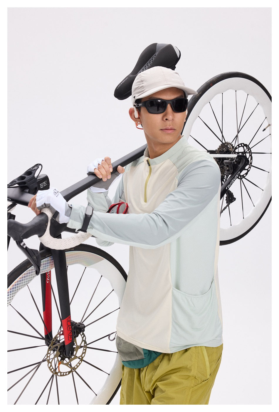 A man in a cream and pale blue cycling top poses beside a road bike, showing the front and side pockets.