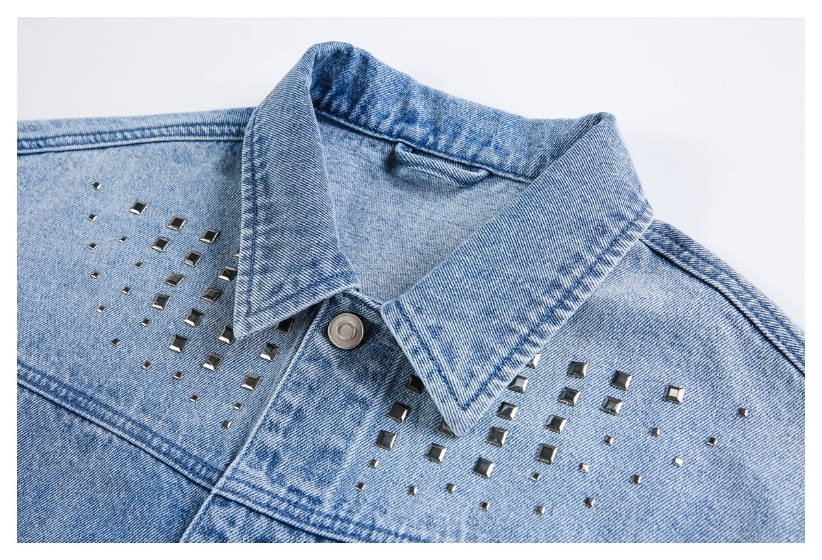 Close-up of a light blue denim jacket collar and chest decorated with dark square metal studs.