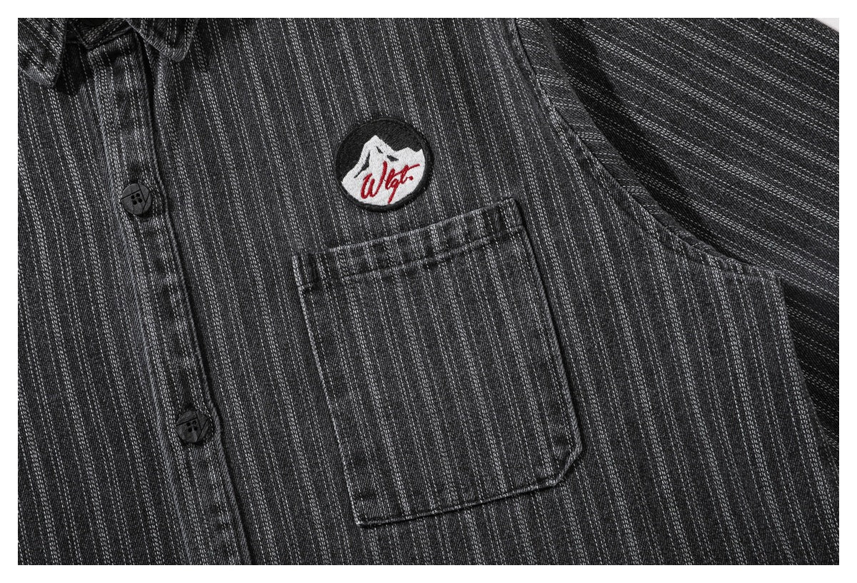 Close-up of the charcoal pinstriped shirt's button placket, chest pocket and embroidered patch.