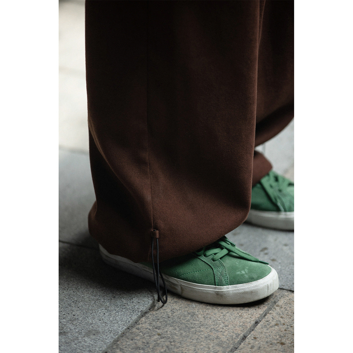 Close-up of brown wide-leg pants with an adjustable ankle cord, worn over a green sneaker.