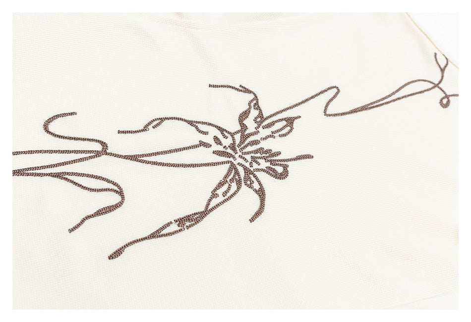 Dark brown floral line embroidery shown close up on ivory shirt fabric.