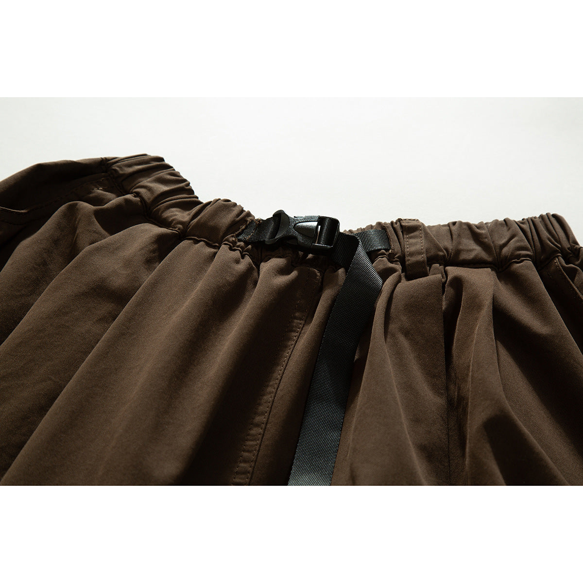 Close-up of a brown skirt's gathered elastic waistband, black buckle, and adjustable strap.