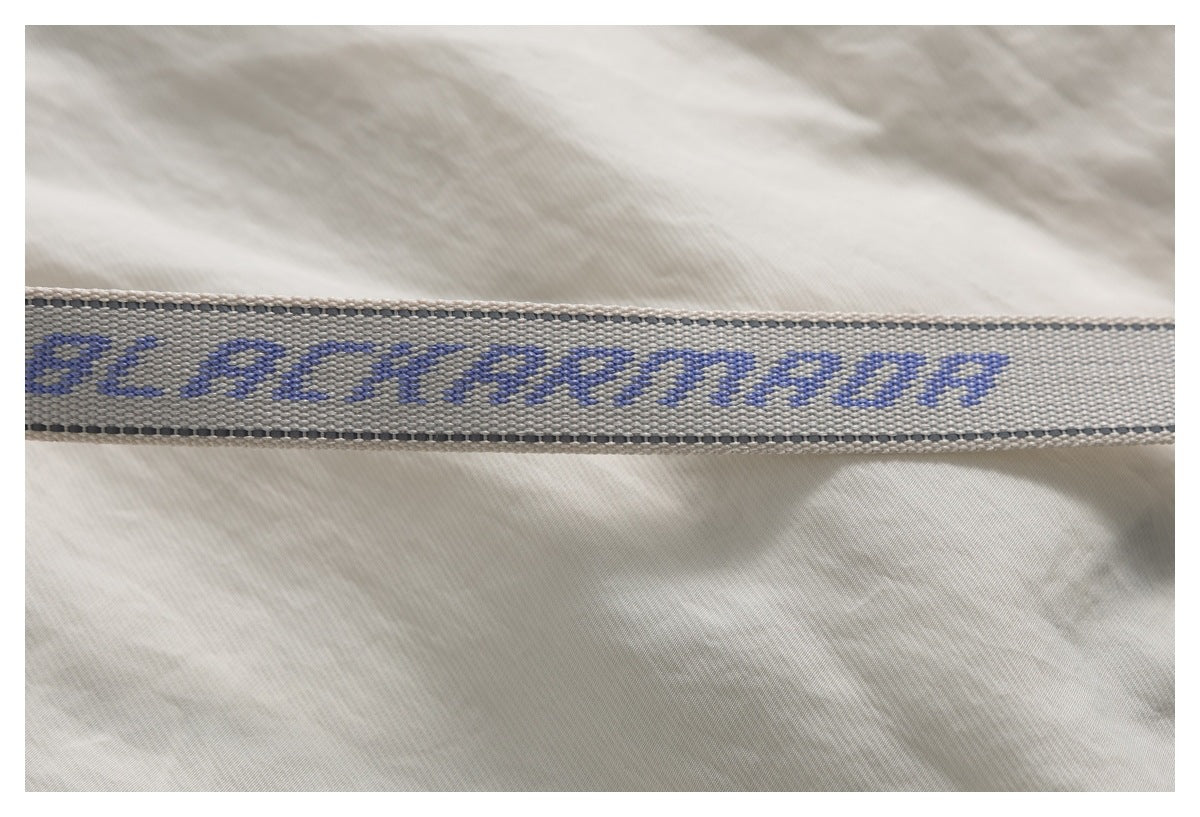 Gray woven strap with blue lettering across cream fabric, shown in close-up.