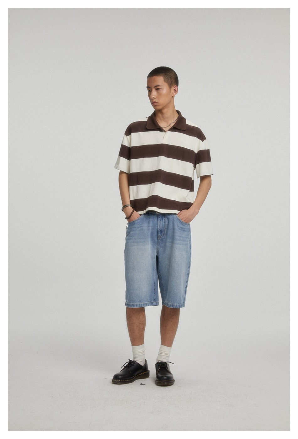 Model wearing a brown-and-cream striped short-sleeve polo and light blue denim shorts, standing at an angle.