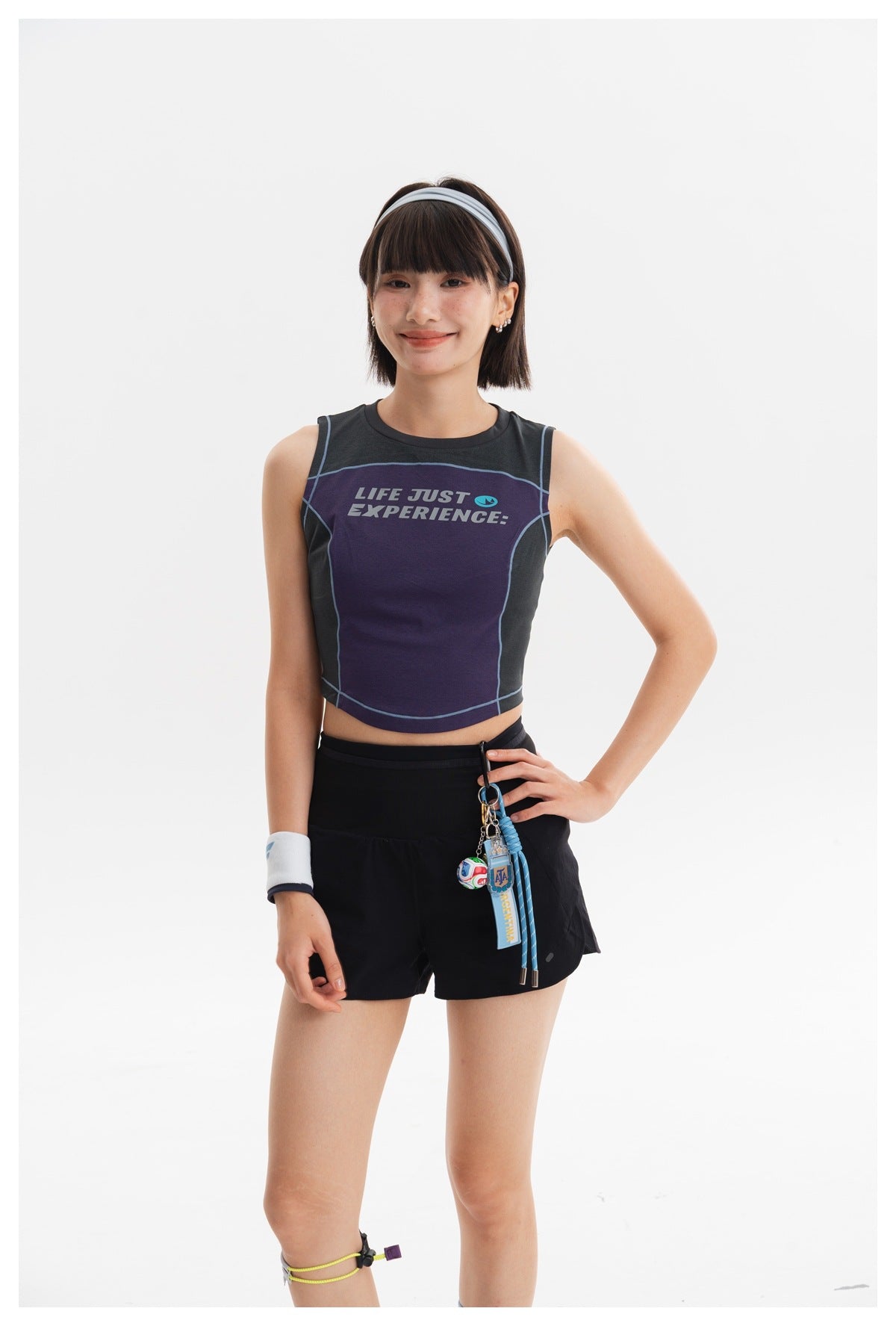 Front view of a model wearing a purple and charcoal graphic crop top with black shorts.
