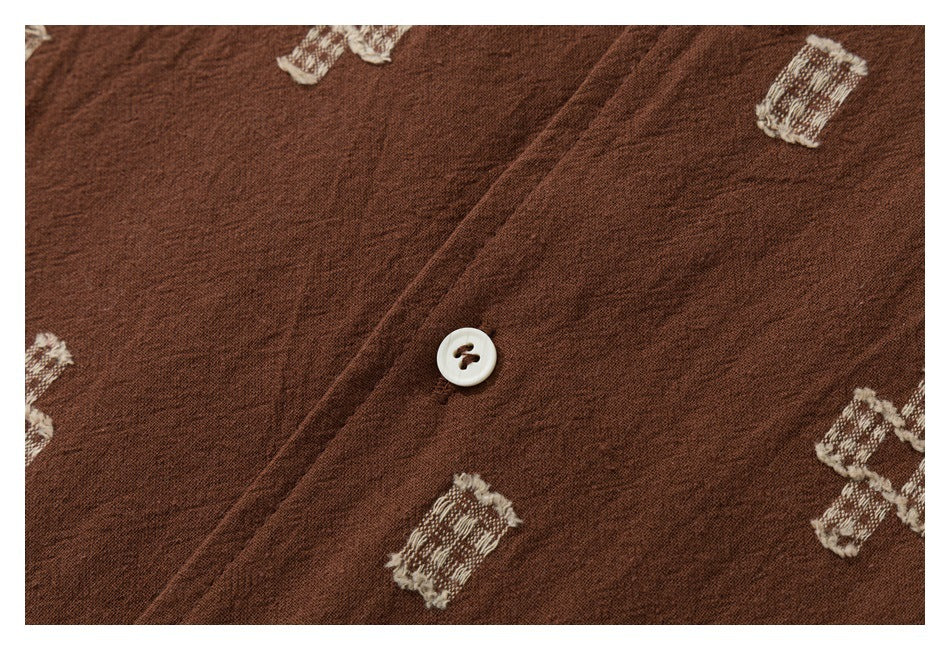 Close-up of a brown garment with cream geometric motifs and a white button on the placket.